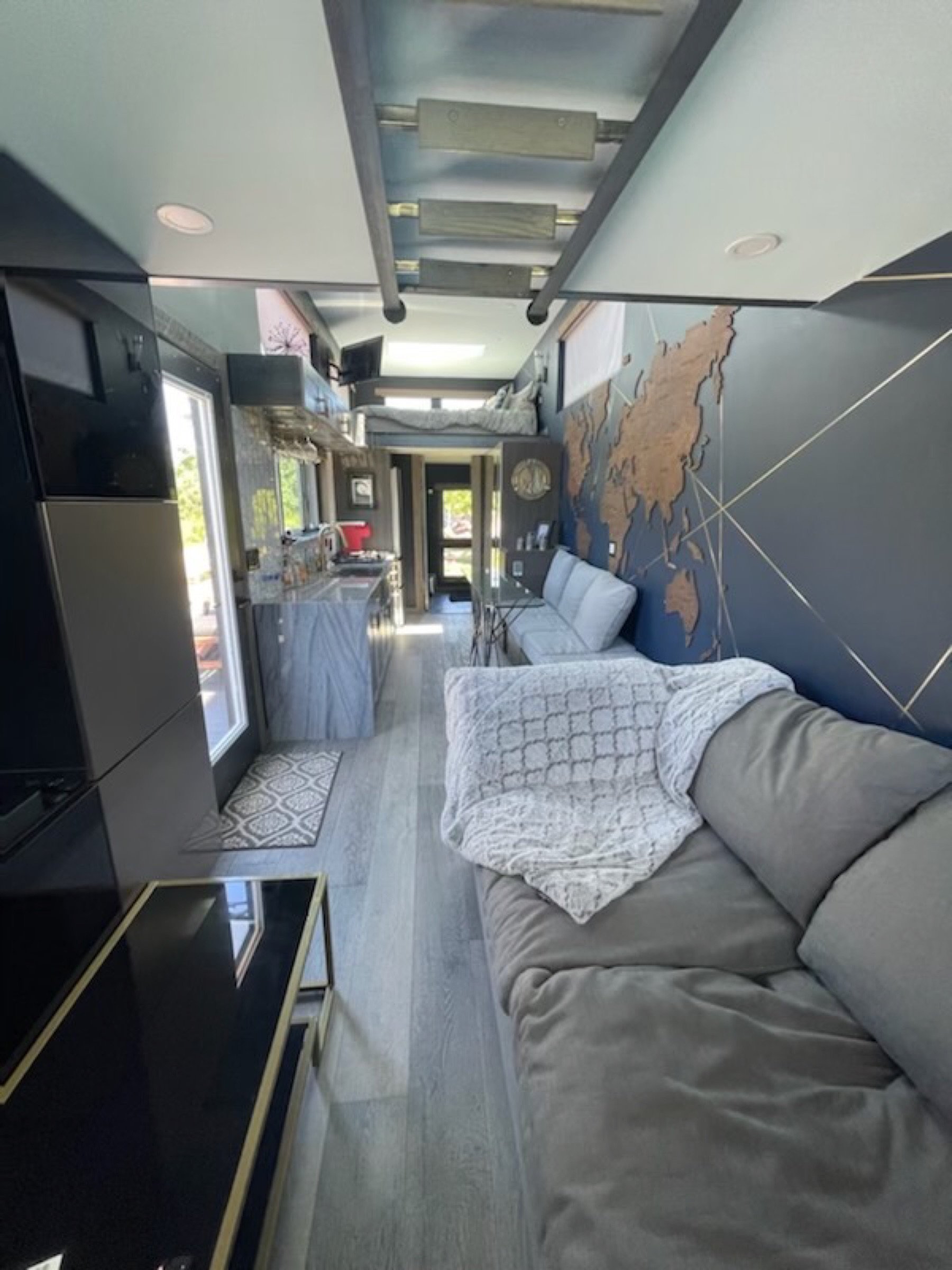 Wide interior view of the compact living zone with sofa seating, kitchenette, and loft sleeping above