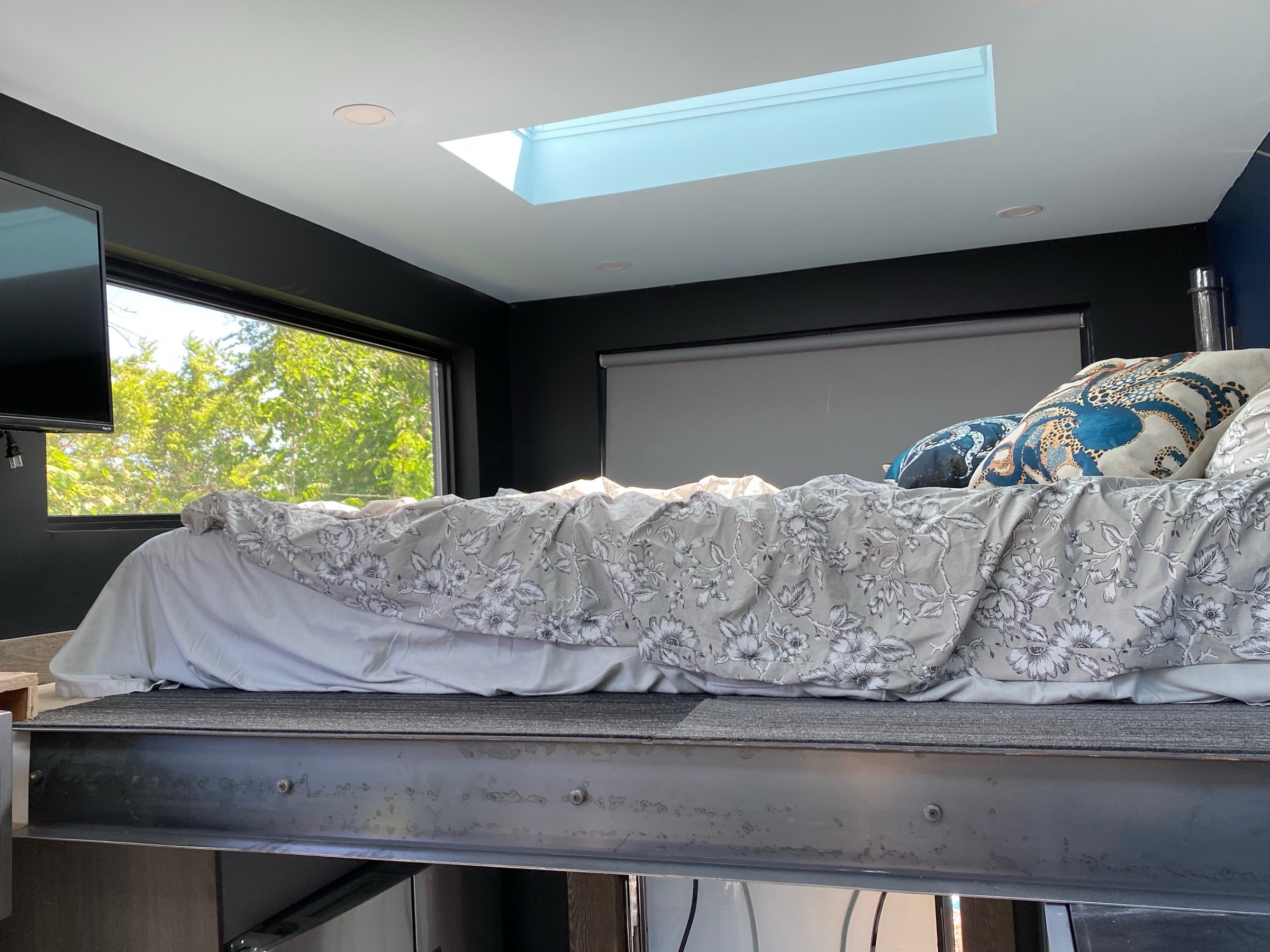 Loft sleeping platform with skylight, dark walls, and built-in bedding